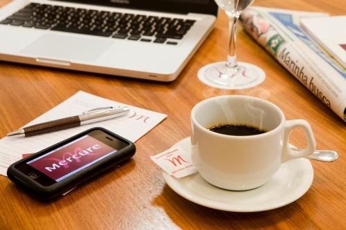 a cup of coffee and a cell phone on a table with a laptop at Mercure Salvador Rio Vermelho in Salvador