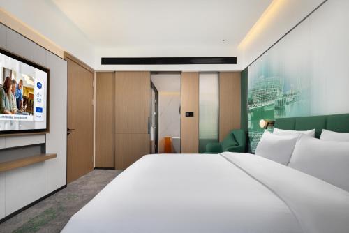 a bedroom with a large white bed and a tv at Hampton By Hilton Dongguan Nancheng Xiping in Baima