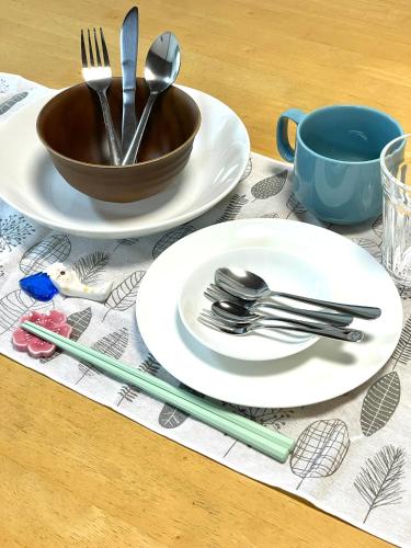 a table with plates and utensils and a bowl at Minpaku SAKURA 民泊 戸建貸切 彦根城まで車10分 無料駐車場 普通2台小型1台 in Hikone