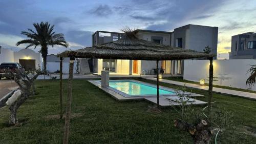 a villa with a swimming pool and a straw umbrella at Villa DEJRBA De LUXE in Houmt Souk