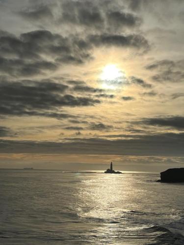 a lighthouse in the ocean under a cloudy sky at The Hideaway Bureau - Islay in Wooler