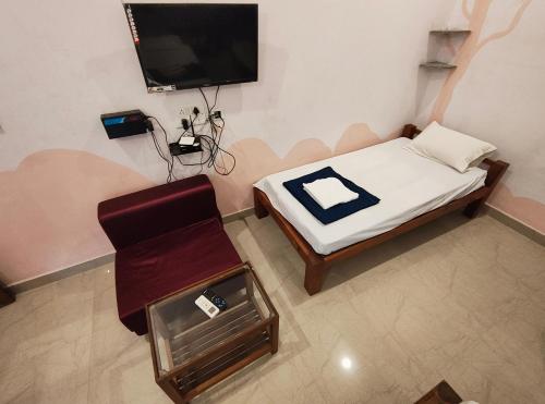 a room with a small bed and a chair and a tv at Art Le Cafe in Auroville