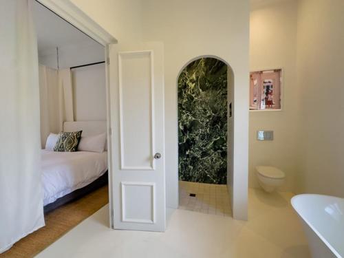 a white room with a bed and a bathroom at Huguenot House in Franschhoek