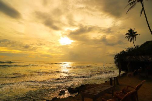 a sunset on a beach with a palm tree and the ocean at Sandakini Home Rest in Ahangama