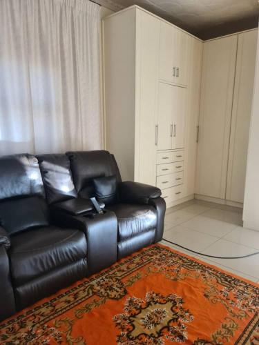 a living room with a black leather couch and a rug at Likhanyile Guest Lodge in Nhlangano