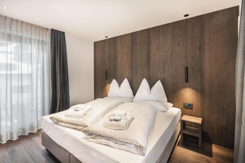 a bedroom with a large white bed with a wooden wall at Aquila Dolomites Residence in Ortisei