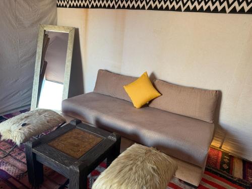 Una habitación con un sofá con una almohada amarilla y un espejo. en Arawan Luxury Desert Camp at Erg Lihoudi, en Mhamid