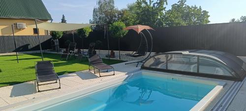 a swimming pool with chairs and an umbrella next to a fence at Zöld Apartmanház in Balatonboglár