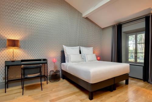 a bedroom with a bed and a desk and a window at La Jasso Hôtel, Maison de Famille in Carcassonne
