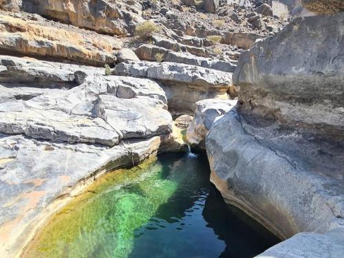 a pool of water in a canyon with rocks at Jabal Shams bayt kawakib in Misfāh
