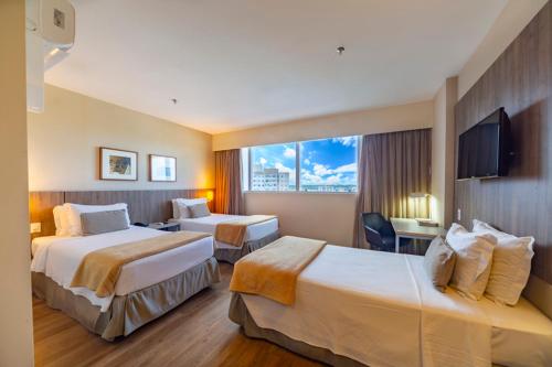a hotel room with two beds and a television at Intercity Salvador Aeroporto in Lauro de Freitas