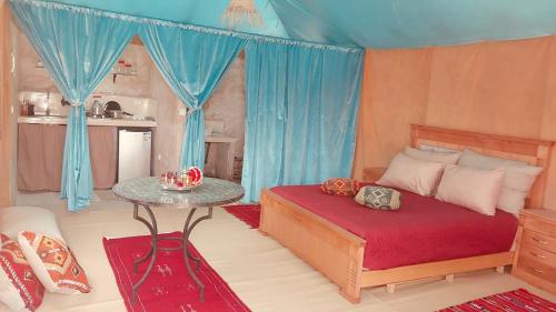 a bedroom with a bed with a table and blue curtains at Ez-zine Glam in El Aadamna