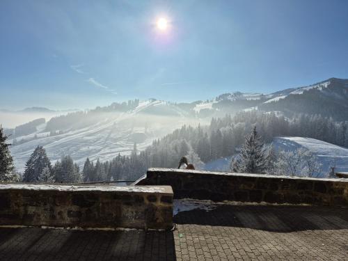 a person sitting on a wall overlooking a snowy mountain at Jugendherberge Bayrischzell-Sudelfeld in Bayrischzell