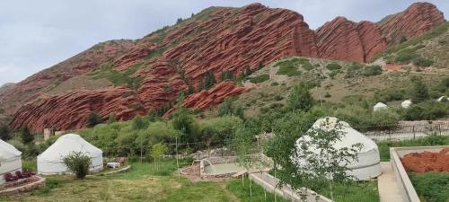 a red rock mountain with trees and white domes at Jhibek in Dzhetyoguz