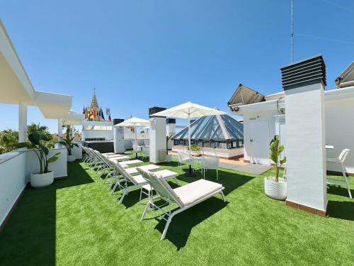 a row of white lounge chairs on a patio with grass at Hotel Apartamentos Marina Luz in Chipiona
