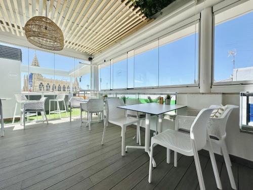 a dining room with white chairs and a table and windows at Hotel Apartamentos Marina Luz in Chipiona