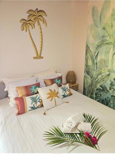 a white bed with colorful pillows and a palm tree mural at Ti Oasis SEAVIEW, Studio Vue Mer à 150m de la plage in Corps de Garde