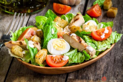 a bowl of salad with chicken and tomatoes on a wooden table at Penzión Svätopluk v Korytnici in Liptovská Osada