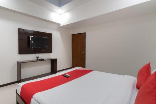 a bedroom with a bed with a red blanket and a television at Hotel O Shivam in Vadodara