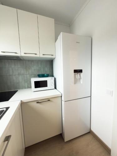 a white kitchen with a refrigerator and a microwave at 103 - Beachside Renovated 1BR apt w private garden in Cambrils