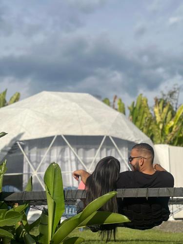 a man and woman sitting on a bench in front of a tent at Orange Eco Villas in Quimbaya