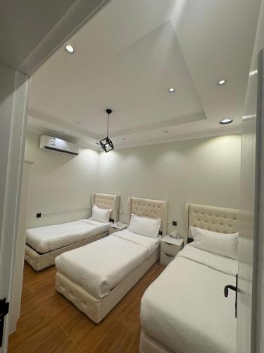 two beds in a room with white walls and wood floors at فيلا فيو السلطان in Abha