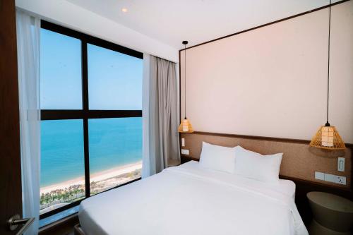 a bedroom with a bed and a large window with the beach at TT Luxury Condotel - Apec Mandala Mui Ne in Mui Ne
