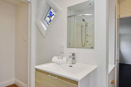 a white bathroom with a sink and a mirror at Hampstead Cottage in Christchurch
