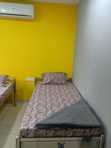 a bed in a room with a yellow wall at Shiv Sai Dormitory in Vadodara