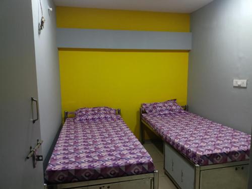 two beds in a room with yellow and yellow walls at Shiv Sai Dormitory in Vadodara