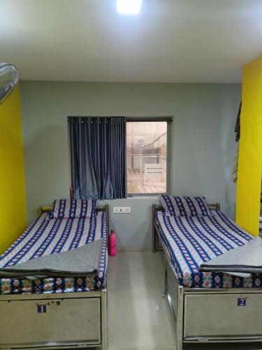 two beds in a room with a window at Shiv Sai Dormitory in Vadodara