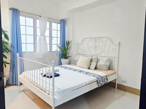 a white bed in a white bedroom with blue curtains at 1 BR-High Floor in Baguio
