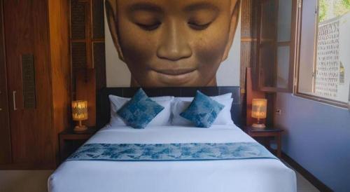 a bed with a picture of a face on the wall at My BanLao Hotel in Luang Prabang