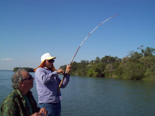 two men standing on a river holding a fishing rod at Cabañas Los Troncos in Ituzaingó