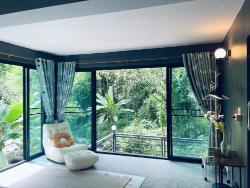 ein Wohnzimmer mit einem weißen Stuhl und großen Fenstern in der Unterkunft Brookside Nest- Lower Floor in Ban Huai Kaeo