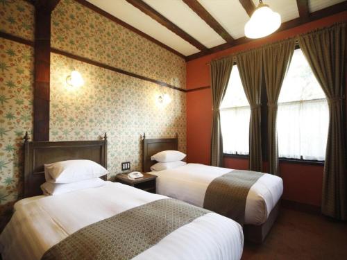 two beds in a room with red walls and windows at Unzen Kanko Hotel in Unzen