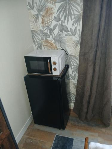 a microwave sitting on top of a black stand next to a curtain at Chambre " Nid Cosy " Charme et Détente chez Fred in Gorron