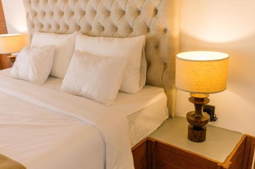a bed with white pillows and a lamp on a night stand at Chaza Oddington in Lindula