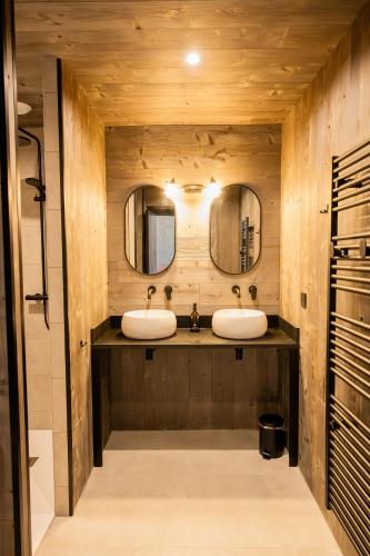 two sinks in a bathroom with wooden walls and mirrors at Domaine du Grand Caugy in Saint-Vigor-le-Grand