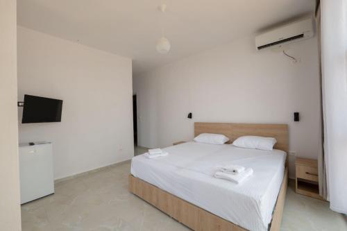 une chambre avec un lit aux draps blancs et une télévision dans l'établissement Brian's Rooms, à Saranda
