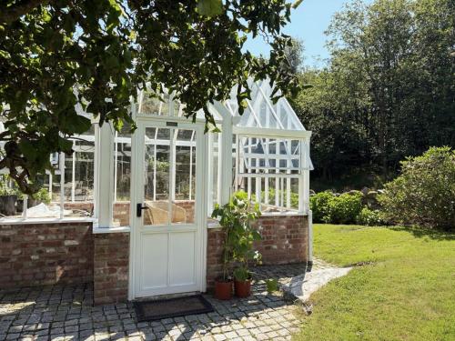a white greenhouse with a door in a garden at Stylish Villa - Boat, Greenhouse & Majestic Oaks in Sørvåg