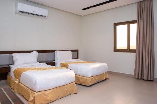 two beds in a room with white walls and a window at Triple Tree Serviced Unites in Al Hofuf