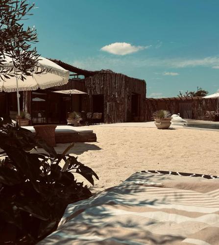 a sandy beach with an umbrella and a building at Domaine FINCA LESSYA, Lodge insolite & SPA in Mauguio