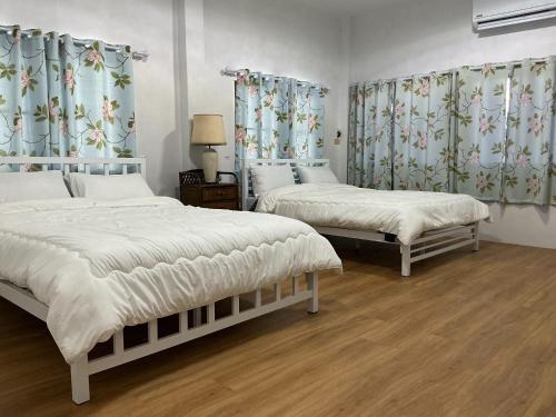 two beds in a bedroom with curtains and wooden floors at Choltara house in Hat Yai