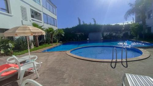 a swimming pool with an umbrella next to a building at Appartement moderne proche de la plage avec piscine in Skhirat