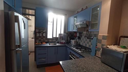 a kitchen with blue cabinets and a refrigerator at Appartement moderne proche de la plage avec piscine in Skhirat