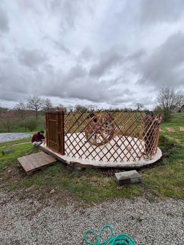 un banc en bois avec une clôture et une roue en bois dans l'établissement Aux Yourtes de La Fabrique, à Saint-Florent-des-Bois