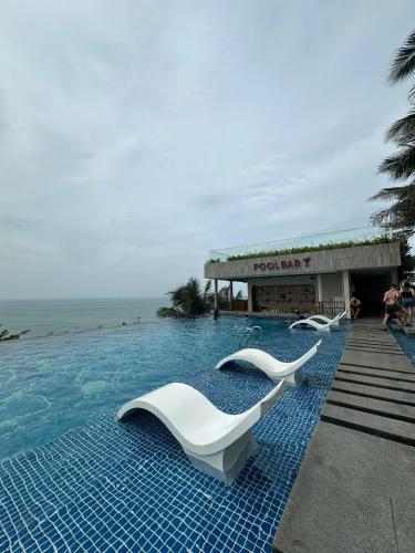 a swimming pool with white chairs in front of a resort at Apec Mandala wyndham Apartment - APEC Mui Ne in Mui Ne