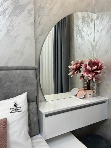 a white dressing table with a mirror and flowers at Apartman Stoiljkovic Vrnjacka Banja in Vrnjci