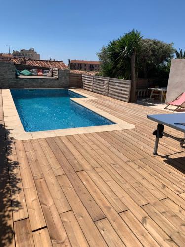 une terrasse en bois avec une piscine et une table dans l'établissement C’est là qu’il faut venir cet été, à Marseille